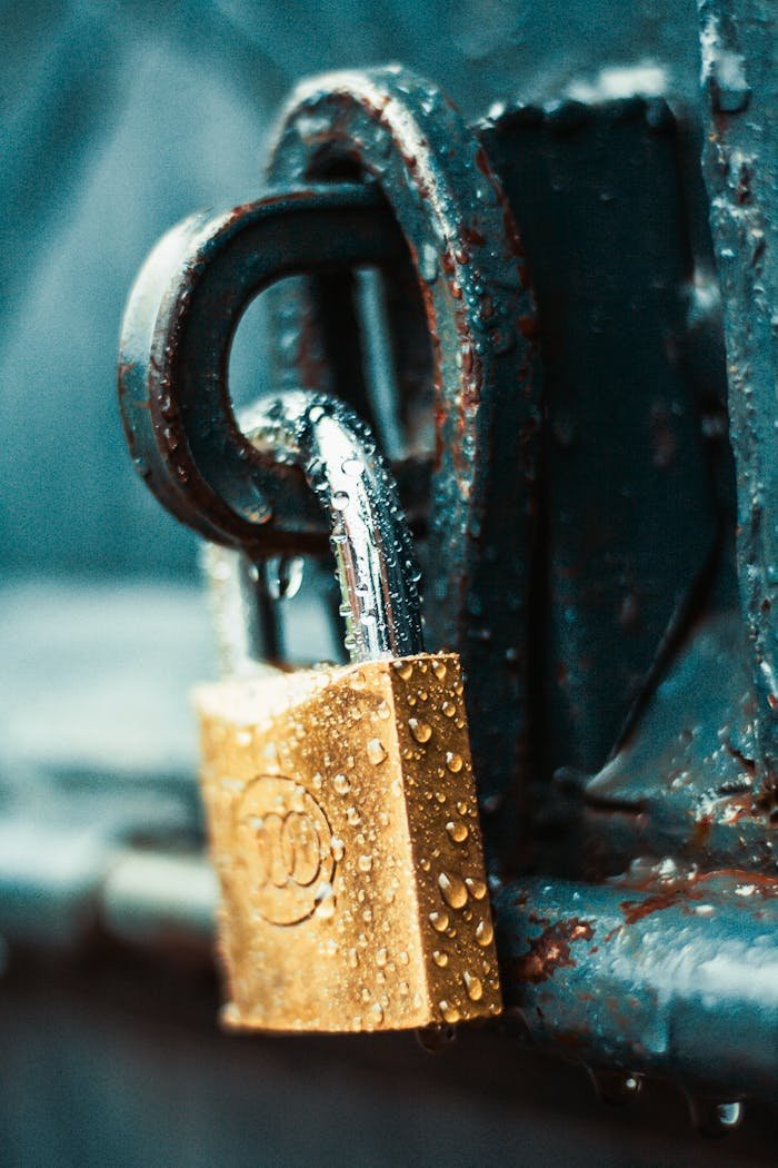 journey A detailed shot of a wet padlock on a rusty metal surface, showcasing textures and water droplets.