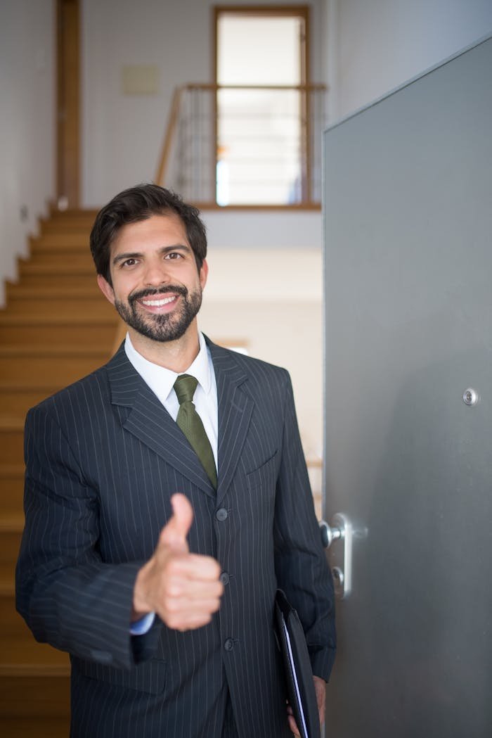 who-we-are Smiling realtor giving thumbs up at open house indoors. Ideal for real estate marketing.